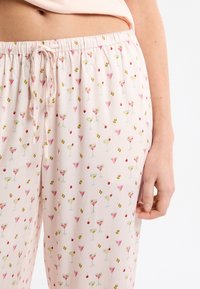 Spodnie od piżamy wykonane z jasnoróżowego materiału z zabawnym wzorem koktajli, wiśni i oliwek. Posiadają elastyczny pas z troczkiem.