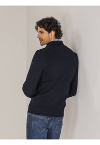 Navyblauer Baumwollmix-Pullover mit gerippten Bündchen und Saum, hoher Kragen und strukturiertem Strickmuster. Getragen mit Denim-Jeans.