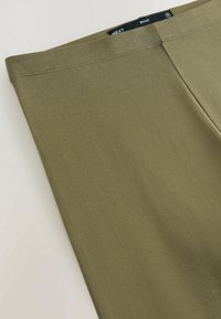 Maslinaste zelene kratke hlače od rastezljivog materijala s glatkom teksturom i čistim linijama. Imaju pojas s oznakom koja označava marku i veličinu.