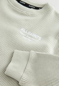 Maglione grigio chiaro a maglia waffle con colletto girocollo, polsini a coste e dettagli del logo ricamati vicino al collo.