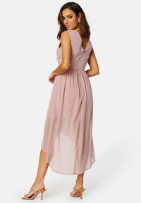 Różowa midi sukienka z dekoltem w kształcie V, plisowaną spódnicą, rękawami typu cap oraz zwiewnym dołem. Połączona z przezroczystymi obcasami.