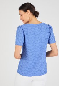Blauw gestructureerd T-shirt met korte mouwen, gekenmerkt door ingewikkelde bloemmotieven, ronde halslijn en een licht ontspannen pasvorm. Achteraanzicht weergegeven.