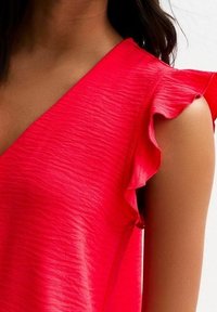 Rode gerimpelde top met een v-halsontwerp, voorzien van textiel met structuur en vrouwelijke schouderaccenten. Close-up toont de details van het materiaal.