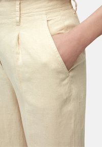 Beige linnen broek met gepliseeerde voorzijde, zijzakken en een gladde textuur. Heeft een getailleerde pasvorm en gestikte tailleband.