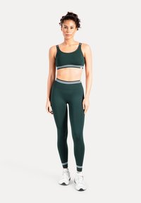 Mörkgrönt sport-bh- och legging-set med vita ränder vid midjan och fållen, tillverkat av stretchigt material, designat för idrottskläder.