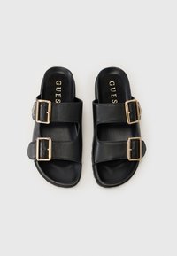 Sandale slide din piele neagră, cu două curele și catarame aurii, talpă plată și o textură netedă. Potrivite pentru ținute casual.