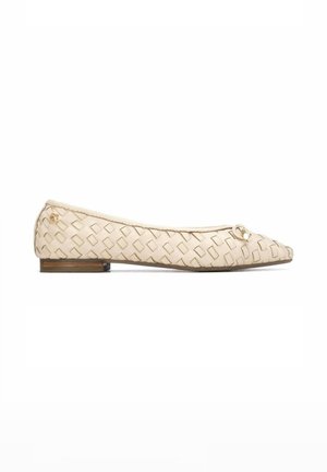 Zapato plano de cuero beige tejido con tacón pequeño y lazo decorativo en la puntera puntiaguda, mostrado en perfil lateral sobre fondo blanco.