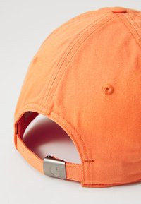 Orange cotton cap with a textured finish, featuring a metal adjuster at the back and four ventilation holes along the side.