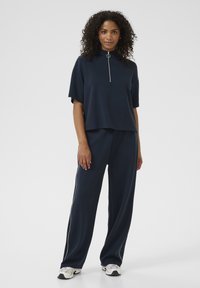 Navy crop top with a high collar and short sleeves, featuring a zipper front and a silver ring pull. Paired with loose-fitting pants with side stripes.