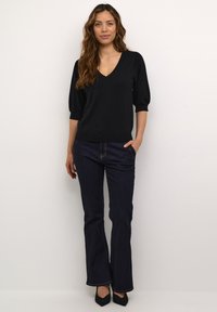 Top en tricot noir avec décolleté en V et manches bouffantes, associé à un jean flare bleu foncé. Les chaussures comprennent des escarpins noirs à bout pointu.