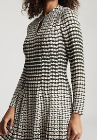 Langärmliges Kleid mit tailliertem Oberteil und ausladendem Rock, das ein geometrisches Schwarz-Weiß-Muster und einen Schlüssellochausschnitt aufweist.