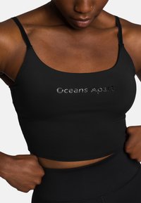 Zwarte cropped tanktop van gladde stof, met een vierkante halslijn en dunne bandjes. "Oceans Apart" is subtiel op de voorkant geperst.