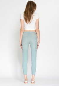 Jasnoniebieskie obcisłe dżinsy z lekko postrzępionymi nogawkami, z dwoma tylnymi kieszeniami i minimalistycznymi detalami szwów. Zaprojektowane dla dopasowanej sylwetki.