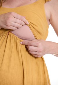 Senfgelbes Kleid mit einem strukturierten, zerknitterten Design. Das Handziehen des Stoffes zeigt eine hellpinkfarbene Innenlage, die mit einem Reißverschluss gesichert ist.