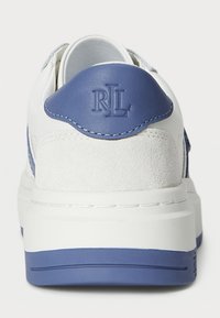 Hvit sneakers med blå lær- og semsket skinn detaljer, glatt tekstur, rund form, hevet hæl, og en logo preget på baksiden.