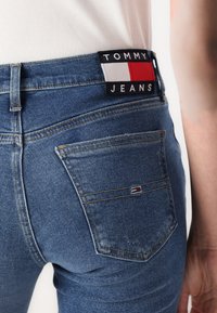 Jeans in denim blu con un design aderente, dotati di una tasca posteriore e di un'etichetta del marchio con elementi rossi, bianchi e blu sulla cintura.