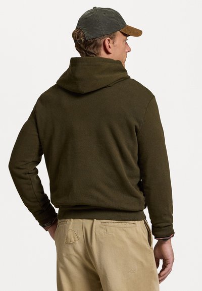 Haut à capuche vert foncé avec poche kangourou, poignets et ourlet côtelés. Associé à un pantalon khaki, présentant un tissu texturé et un design simple.