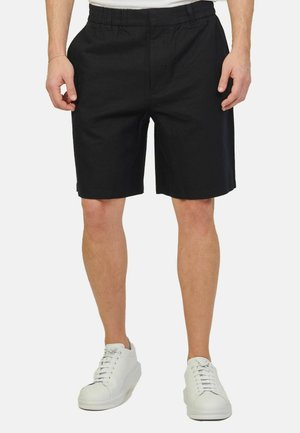 Pantaloni corti neri con vita elasticizzata, caratterizzati da una texture liscia e una vestibilità rilassata, abbinati a sneakers bianche.