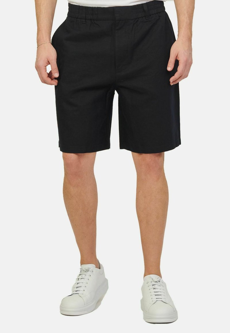 Pantaloni corti neri con vita elasticizzata, caratterizzati da una texture liscia e una vestibilità rilassata, abbinati a sneakers bianche.
