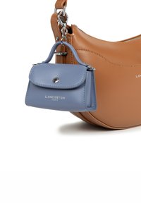 Piccola borsa a tracolla in pelle blu con manico superiore, attaccata a una borsa a spalla più grande in pelle beige tramite un gancio d'argento.