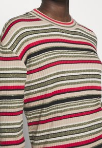 Rybkovaný svetr s vodorovnými pruhy v červené, zelené, černé a béžové barvě, s třpytivou texturou a kulatým výstřihem.