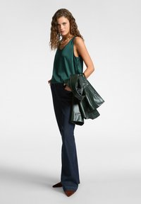 Canotta di raso verde scuro, jeans in denim scuro svasati e giacca di pelle verde scuro. Tacchi a punta marroni completano l'outfit.