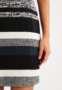 Robe en tricot avec des rayures horizontales noires, blanches et bleu foncé, présentant des textures variées et une silhouette ajustée.