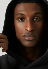 Czarna bluza z wysokim kołnierzem, z przednią kieszenią i sznurkami do regulacji. Zbliżenie na męskiego modela z krótkimi włosami i neutralnym wyrazem twarzy.