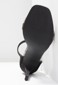 Sandale à talon haut avec une tige en daim noir et une bride contrastante à imprimé serpent. Semelle noire unie avec texture nervurée et détail logo.