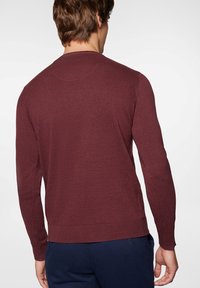 Bordowy sweter z długim rękawem, z ribbowanymi mankietami i dołem, o gładkiej teksturze dzianiny i prostym okrągłym dekolcie. Widok z tyłu.