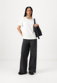 Chemise blanche à manches courtes avec un col en strass, associée à un pantalon large noir à pois blancs. Tenue d'un sac à épaule noir.