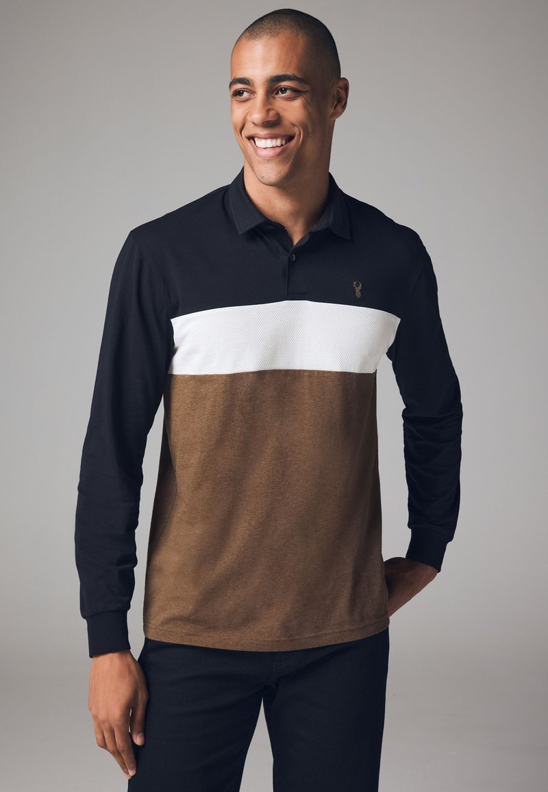 Långärmad polo skjorta med en svart övre del, en vit mellandel med ett texturerat mönster och en brun nedre del.