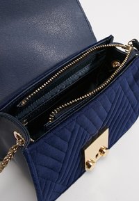 Marineblau gestepptes Handtasche mit goldenen Beschlägen. Verfügt über eine strukturierte Außenseite, eine Kettenriemen und Fächer, die mit einem Reißverschluss und einem magnetischen Verschluss gesichert sind.