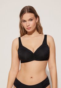 Top de bikini negro con tirantes anchos, con detalles fruncidos en el centro, tejido de textura suave y una forma estructurada adecuada para soporte.