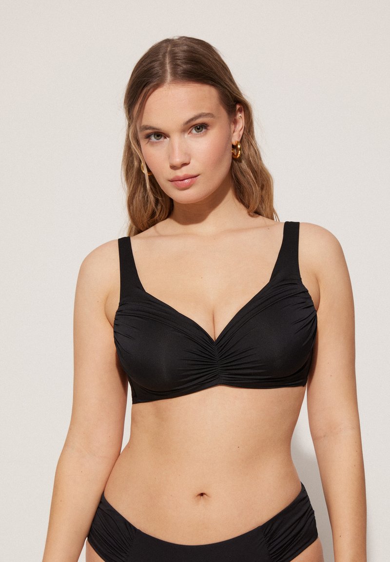 Top de bikini negro con tirantes anchos, con detalles fruncidos en el centro, tejido de textura suave y una forma estructurada adecuada para soporte.