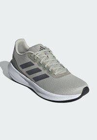 Svetlo šedá atletická obuv s vrchom z textílie, tromi tmavošedými pruhmi, textúrovaným povrchom a bielym stredným pásom s čiernou podrážkou.