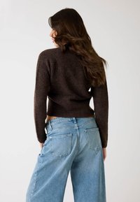 Maglione lavorato a maglia marrone con maniche lunghe e design corto, abbinato a jeans in denim a gamba larga di colore blu chiaro. Texture liscia e vestibilità casual.