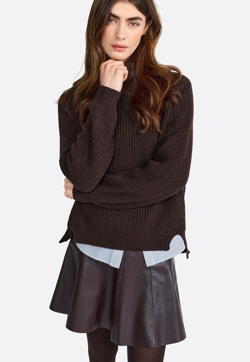 Brown ribbed knit sweater with side slits, layered over a blue and white striped shirt, paired with a dark leather flared skirt.