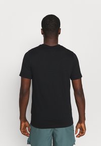 Camiseta negra de cuello redondo con mangas cortas, hecha de una tela suave, con un diseño liso y un corte relajado. Se muestra la vista posterior.