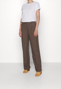 Vit t-shirt med flerfärgade prickar, kombinerad med lösa bruna linnebyxor och gula klacksandaler. Slät tyg, avslappnad passform.