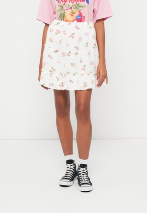 White skirt with a floral pattern, featuring ruffles at the hem and an elastic waistband, paired with black high-top sneakers and white socks.