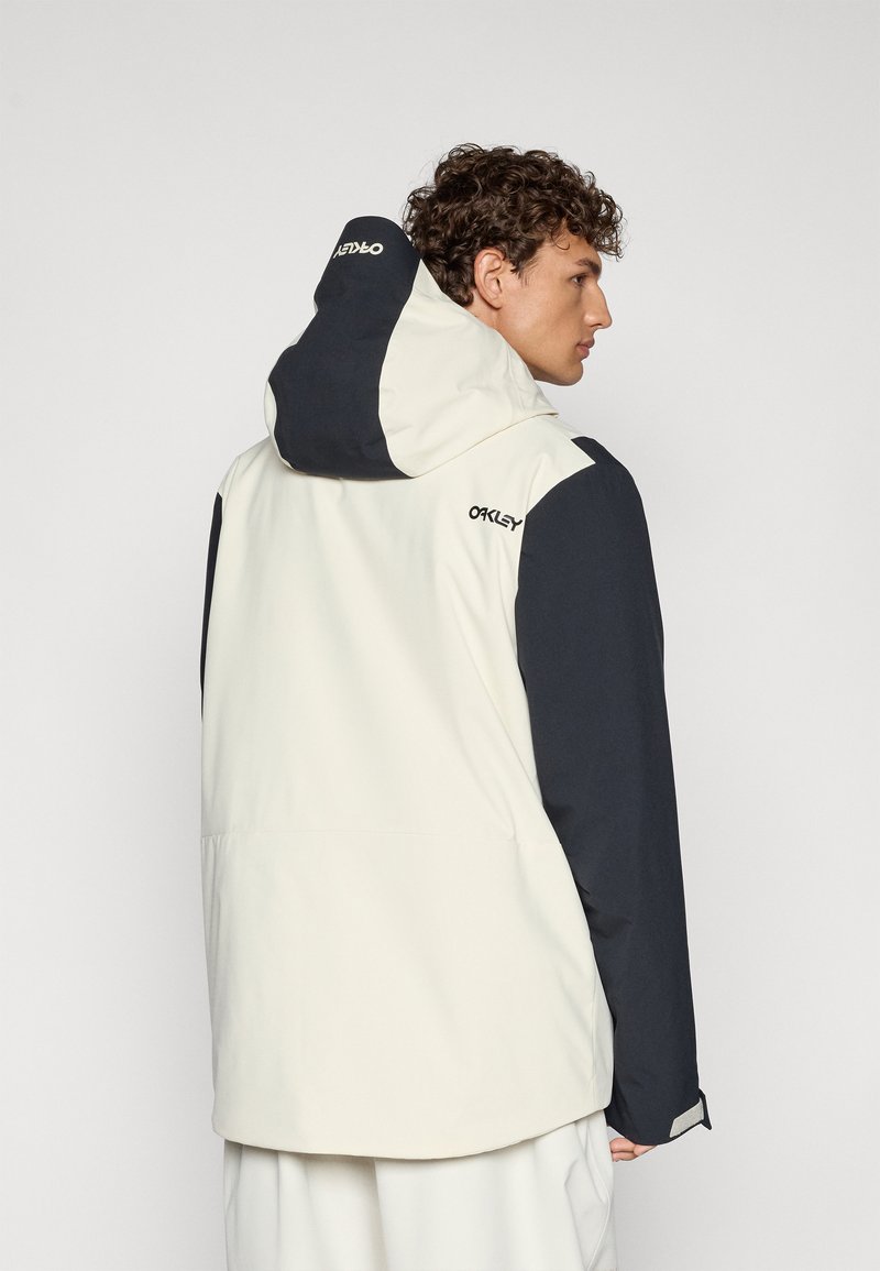 Veste pour homme, avec un design bicolore à corps crème et manches bleu marine, une capuche et des poignets élastiques. Détail du logo dans le haut du dos.