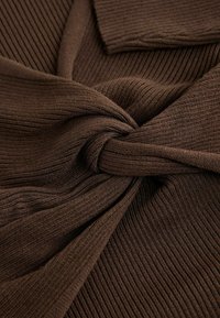 Braunes geripptes Strickgewebe, das in der Mitte gedreht ist, mit einer glatten Textur und einem einheitlichen Muster sowie einem umgeschlagenen Randdetail.