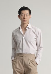 Camisa de botones a rayas de color rosa claro con cuello clásico, combinada con pantalones beiges de cintura alta. Tela suave, corte ajustado, detalles de botones.