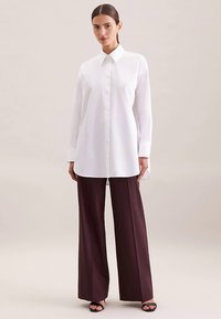 Biała koszula na guziki z kołnierzykiem, długimi rękawami i prostym krojem, zestawiona z ciemnymi bordowymi szerokimi spodniami z wysokim stanem.