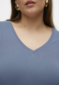 Top a V scollato in tessuto azzurro chiaro, con maniche corte e una trama liscia, abbinato a orecchini statement in oro discreto.