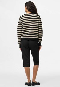 Svart och beige randig jumper med avslappnad passform, rund halsringning och ribbade ärmslut; kombinerad med svarta avkortade byxor och platta svarta skor.