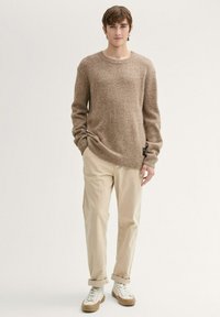 Bruine gebreide trui met een ronde hals, losse pasvorm en geribde manchetten, gecombineerd met beige broeken en witte sneakers met tan accenten.