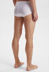 Hvide bomuldsunderbukser med ribbet tekstur, der har en blød elastisk talje og en tætsiddende pasform. Vist fra ryggen, som viser detaljer om benene.