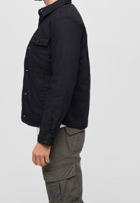 Svart vävd jacka med spetsig krage, framlapp och knäppning. Texturerat tyg, skräddarsydd passform och avslutade ärmslut.